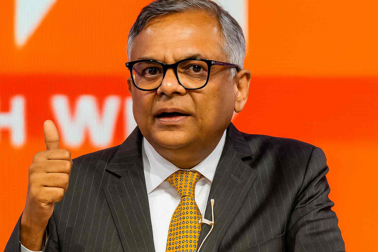 N Chandrasekaran smiling at a Tata Sons board event, symbolising continuity and innovation under his leadership, with visual hints of semiconductor chips, EV cars, and Air India planes in the background.